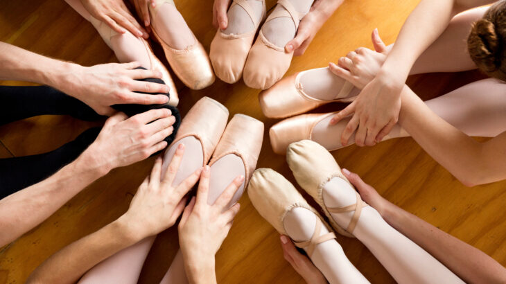 Overhead view of ballerinas holding feet while exercising in ballet studio