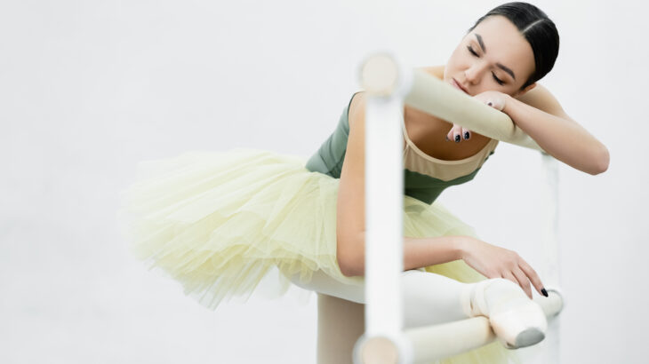 ballerina with closed eyes stretching leg on barre while exercis